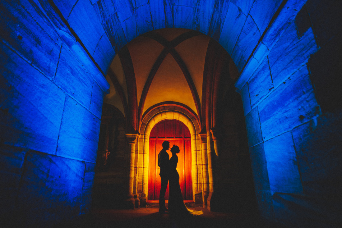 Silhouette eines Hochzeitspaars vor beleuchtetem Torbogen mit blauem und warmem Licht - fotografiert von Rossi, Hochzeitsfotograf Gießen