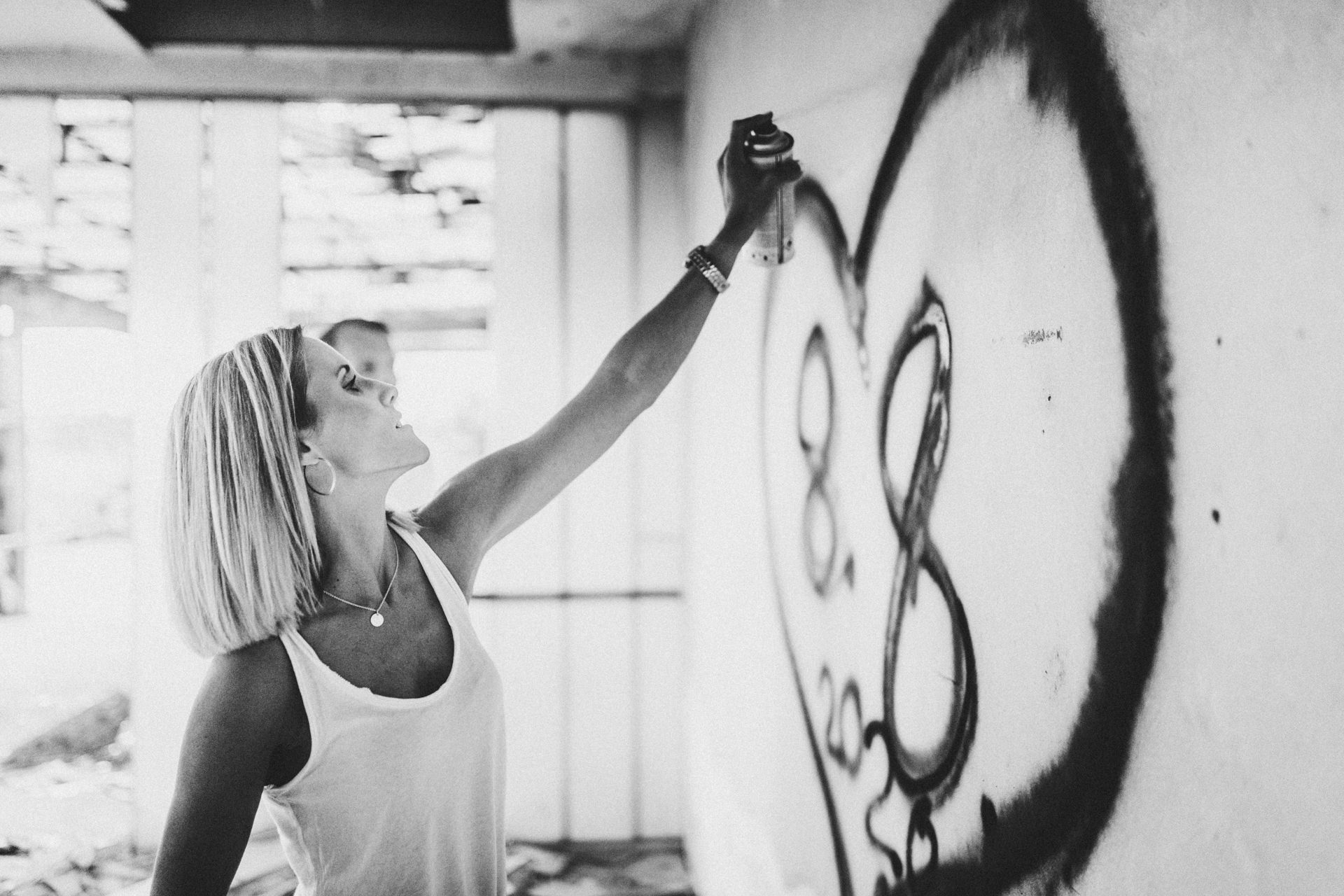 Kristina sprüht bei einem Paarshooting nahe Hungen mit einer Spraydose an eine alte Wand mit Graffiti