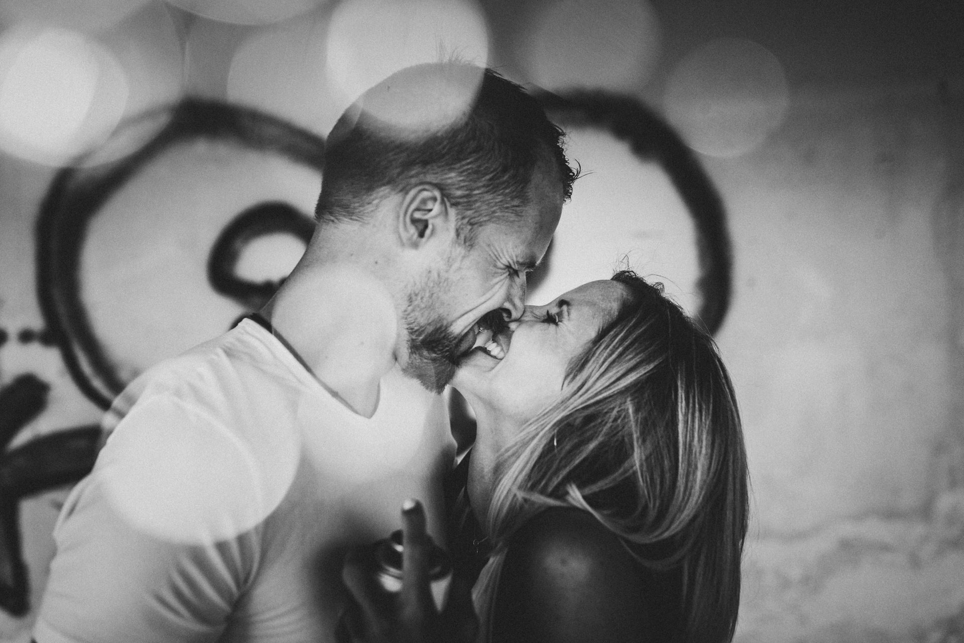 Kristina und Markus stehen eng beieinander bei Paarbildern vor der Hochzeit im Lost Place, mit Graffiti und hellen Lichtpunkten im Vordergrund
