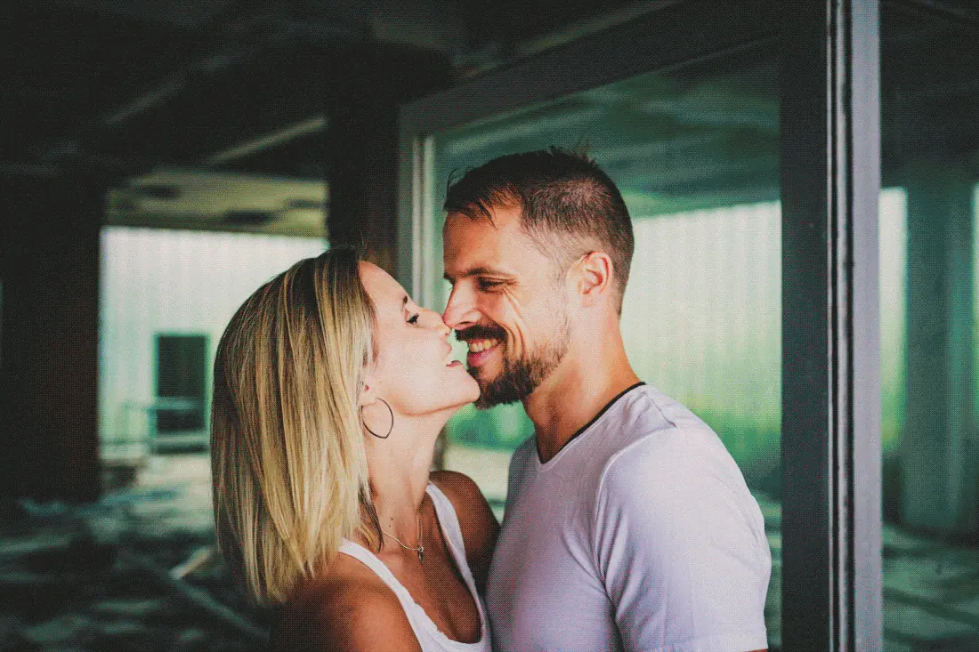 Kristina und Markus stehen eng beieinander bei Paarbildern vor der Hochzeit im Lost Place, mit dunklem Raum, Glasflächen und grünlichem Licht im Hintergrund