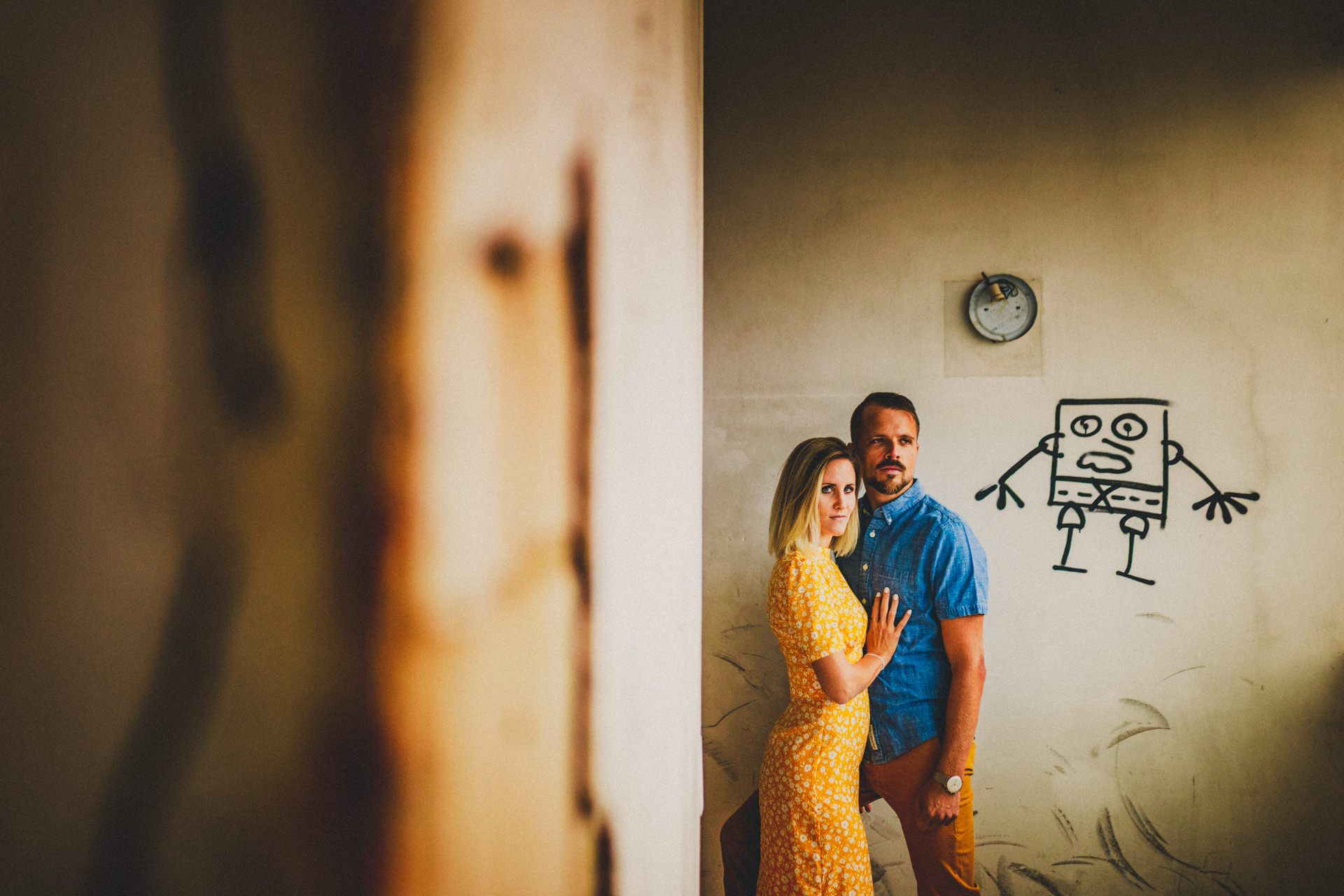 Kristina und Markus stehen nah beieinander vor einer Wand mit Graffiti-Figur in einem verlassenen Gebäude