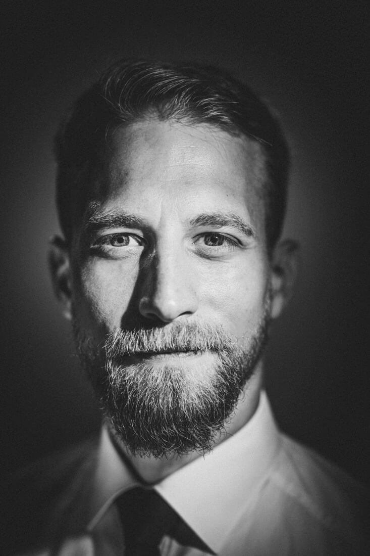 Schwarzweißes Bewerbungsfoto bei Gießen: intensives Portrait eines Mannes mit Bart, Hemd und Krawatte vor dunklem Hintergrund