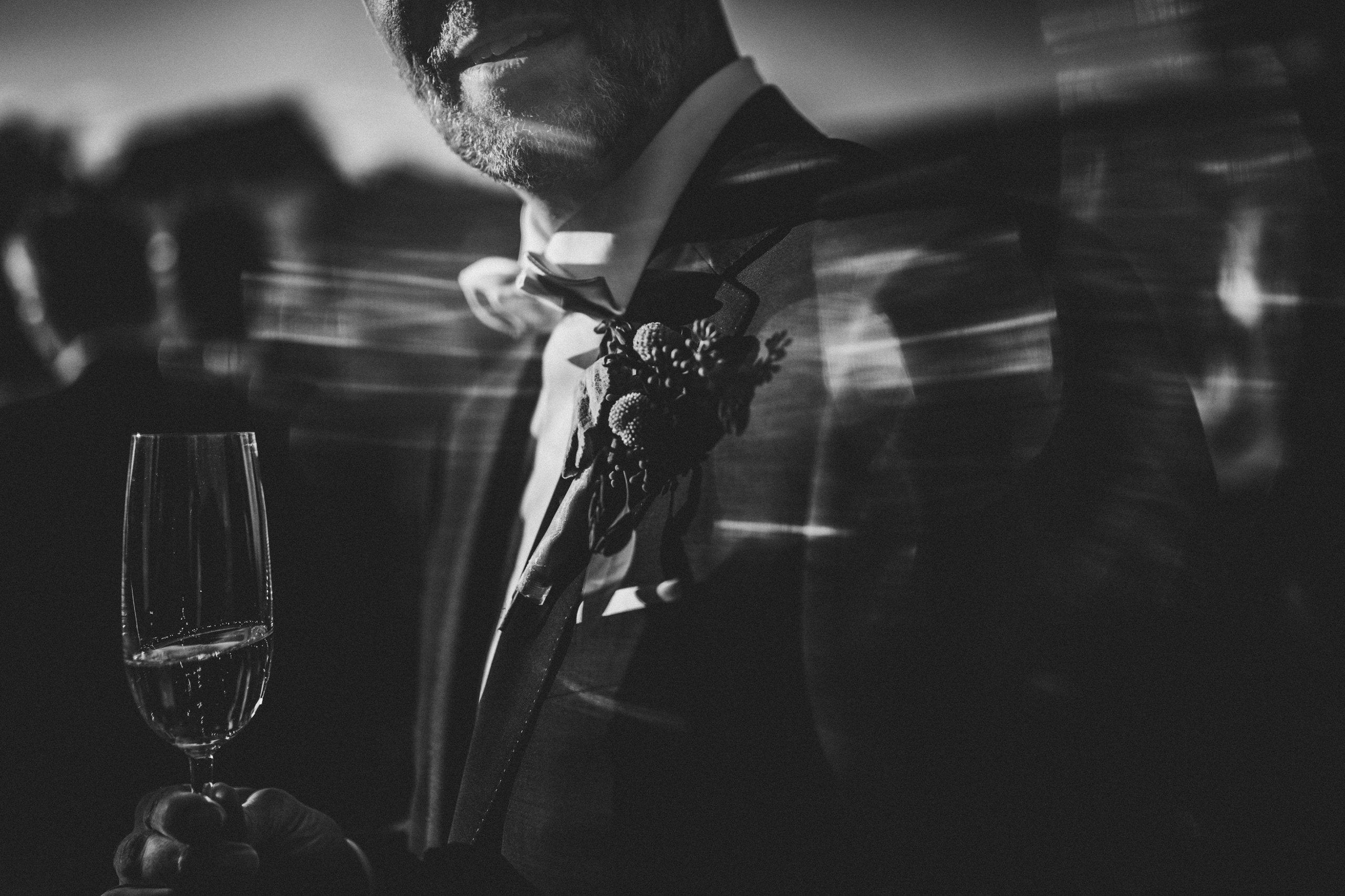 Bräutigam mit Sektglas im Gegenlicht, umgeben von Bewegungsunschärfe der Gäste - fotografiert von Rossi